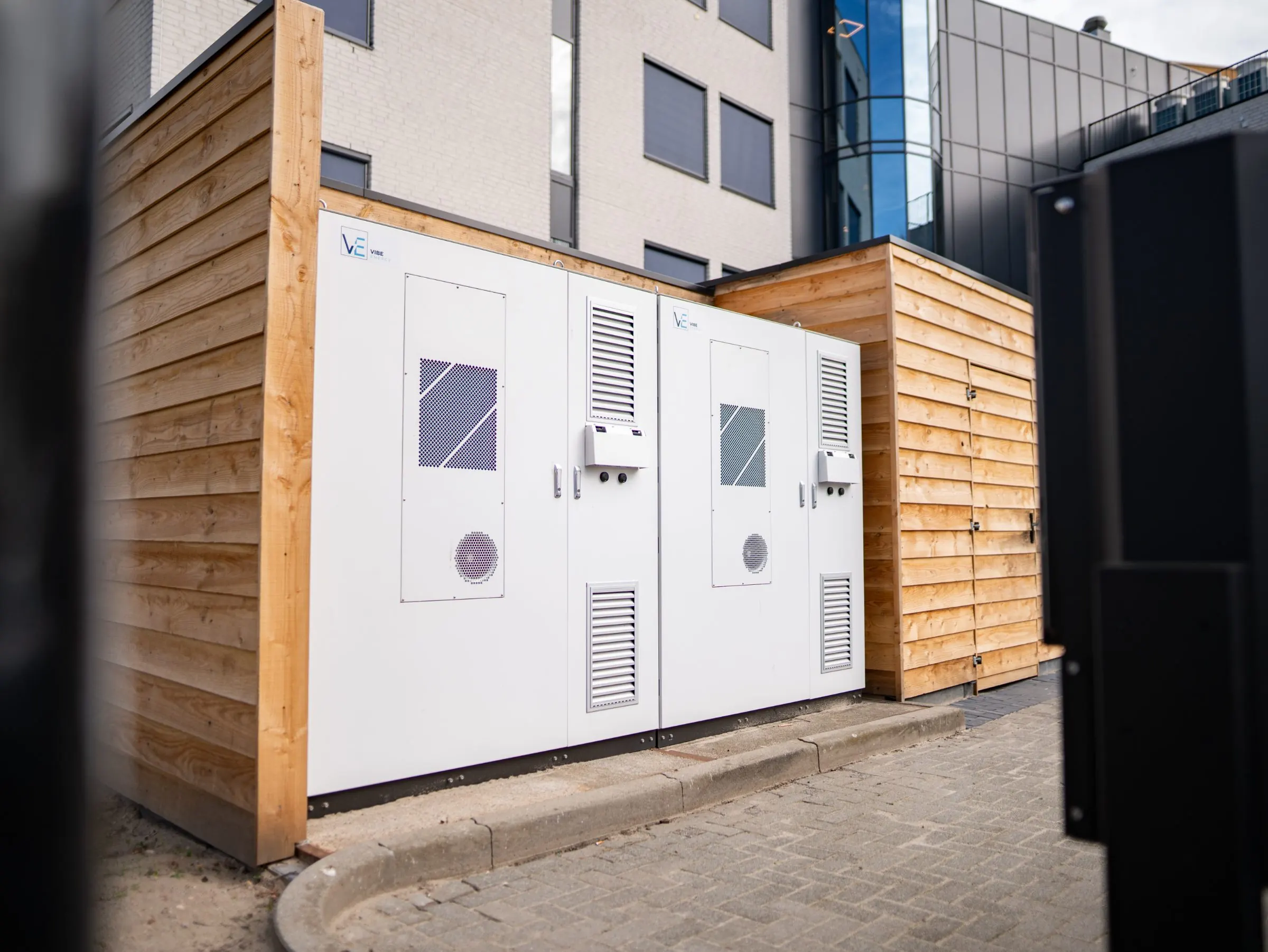 Twee batterijkasten van Vibe Energy in een houten omkasting naast een bedrijfspand
