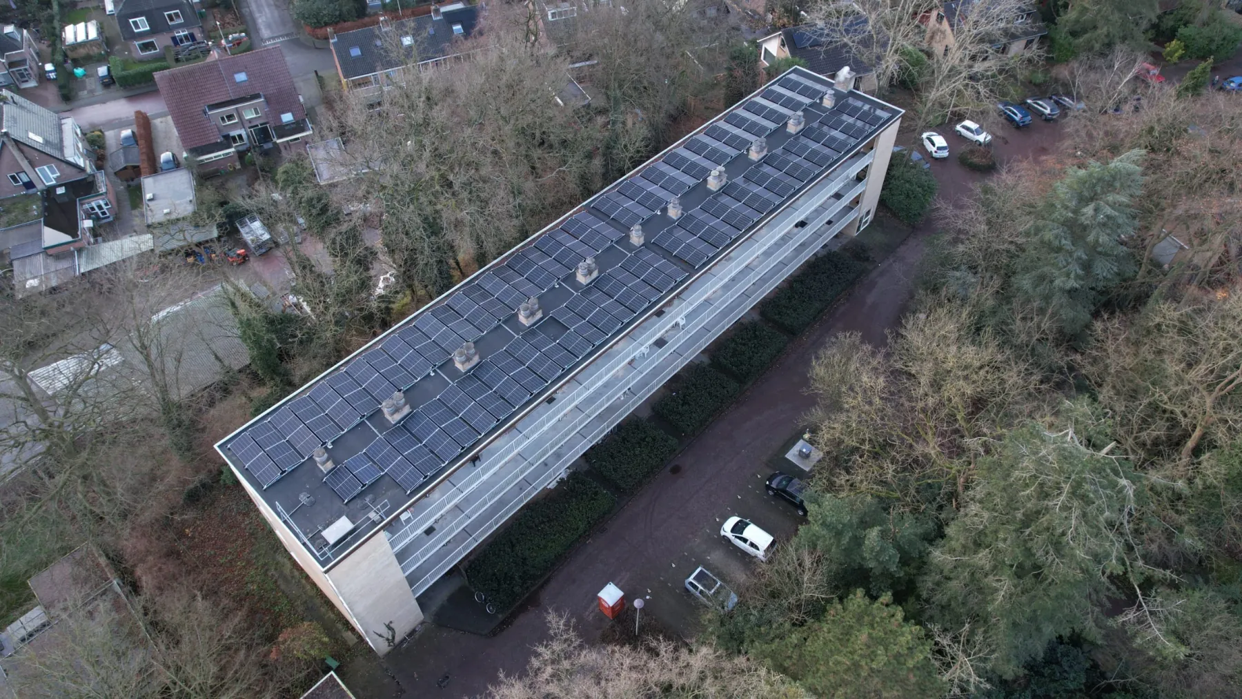 Luchtfoto van het wooncomplex aan de Ketsheuvel in Renkum: één langgerekt gebouw met galerijen, waarvan het dak over de volle lengte met zonnepanelen is belegd