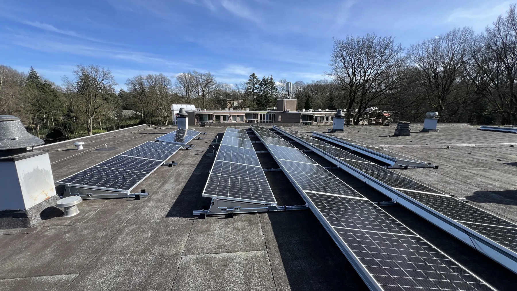 Rijen zonnepanelen op het platte dak van de Kwakkenbergflat in Nijmegen, met bomen op de achtergrond