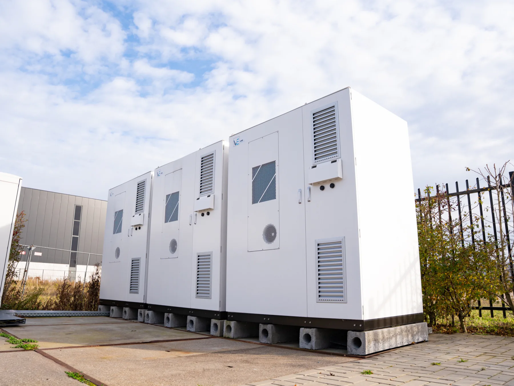 Drie batterijkasten van Vibe Energy op betonnen voeten op het terrein naast een bedrijfspand